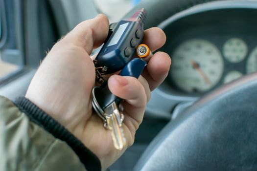 the hand of the person who is in the car holds the disassembled alarm keychain and a new battery for replacement