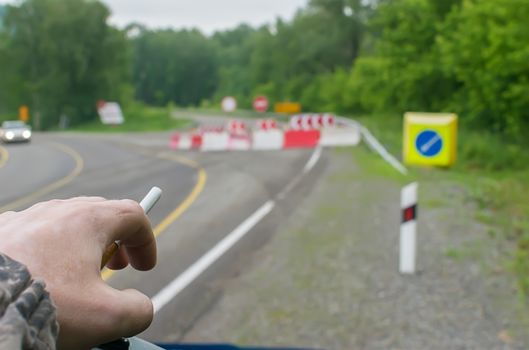 close up, hand of a man with a cigarette, getting out of a car against the background of a blocked road and bypass signs