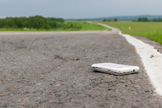 View of a mobile phone lying on the asphalt on a country road in cloudy weather