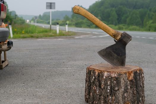 view of the ax, which is stick in a wooden chock on the background of a country road