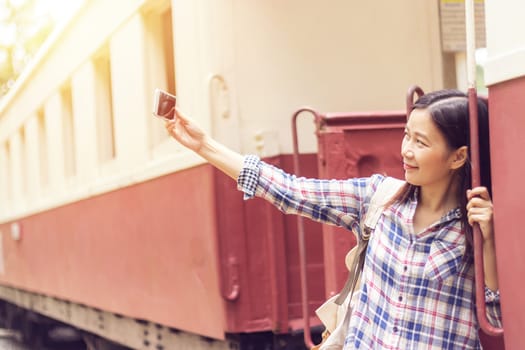 happy young Asian traveller woman taking selfie photo from mobile phone at train station while traveling