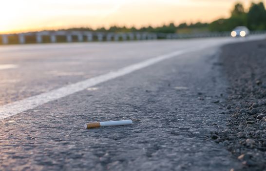 view of cigarette lying on the asphalt on a country road on the background of the leaving car