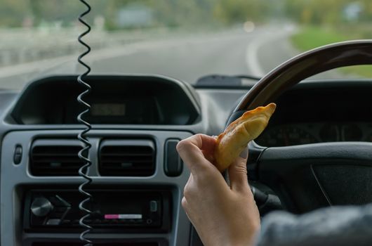 Closeup, of female hand holding a bun behind the wheel of the car in motion on highway