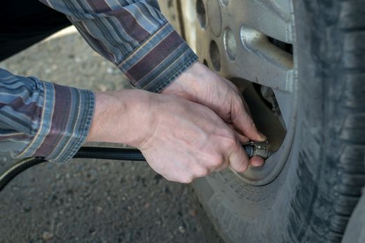 human hands insert the hose of the car pump to pump air into the wheel of the car