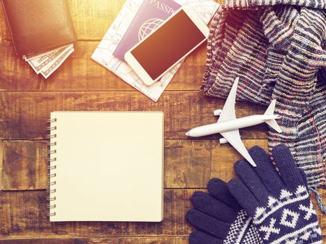 flat lay of passport ,mobile phone , plane model , scarf , gloves and traveler's accessories items on wooden background with blank paper for copy space. travel and vacation concept