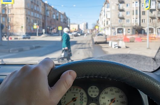 view from the car, the driver hand on the steering wheel of the car, located opposite the pedestrian crossing and pedestrians crossing the road