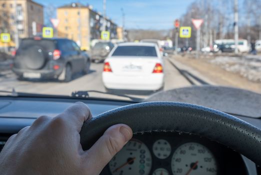 the driver hand on the steering wheel of a car against the background of a street with cars standing in a traffic jam at an intersection with a traffic light