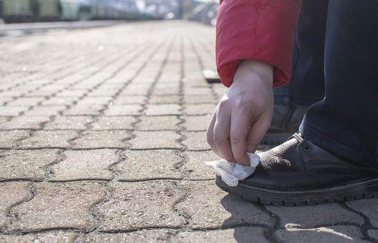 a man cleans shoes, boots with a wet cloth, a rag, while on the platform of a railway station against the background of rails, tracks and freight cars