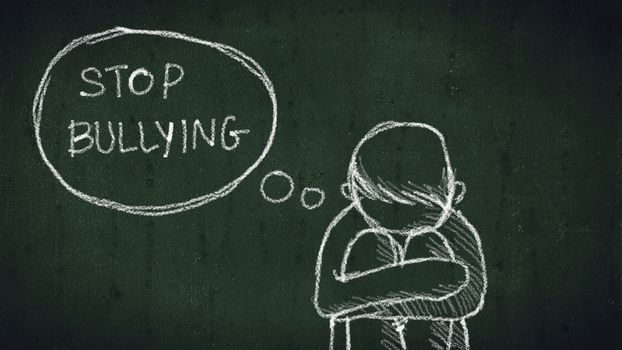 sad young boy sitting on the floor with text stop bullying written with chalk on chalkboard. social problems of humanity