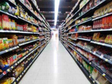 abstract blurred supermarket aisle with colorful goods on shelves with blurry customer at cashier for background