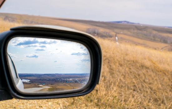 landscape in the rear view mirror of the car road and village in spring