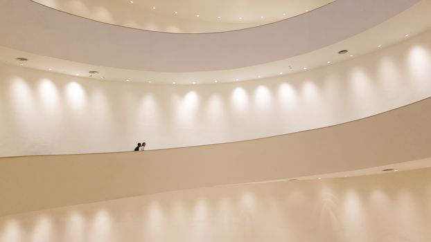 white spiral staircase with white wall with spotlight and people walking