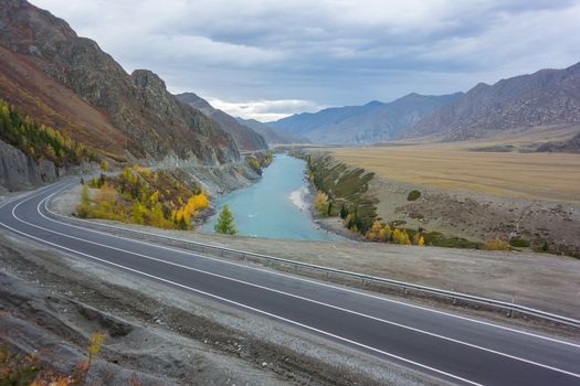 autumn landscape of asphalt road in a mountain valley with a turquoise river