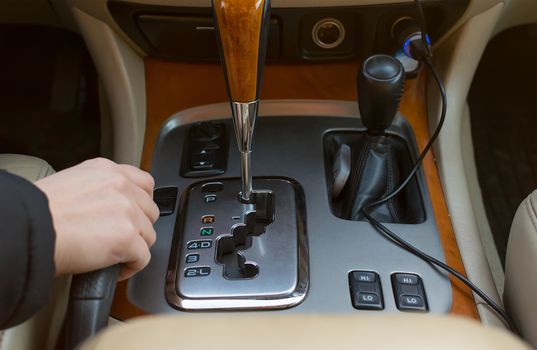 The hand of the driver of the car holding the brake lever, on the background of the automatic transmission controls, close-up view