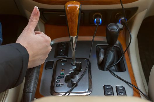 human hand with the symbol "finger up" in the car, near the panel with automatic transmission, closeup