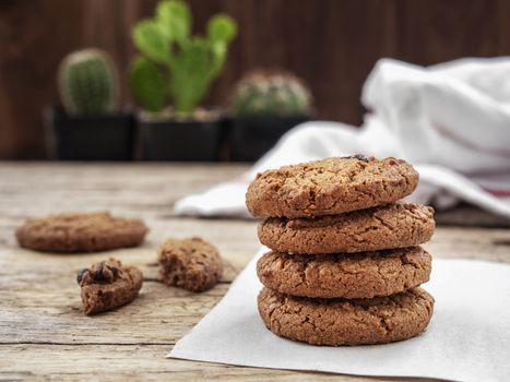 stack of chocolate chip cookies on white napkin paper on wooden table decorate with cactus at background