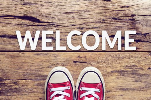 welcome sign text on wooden floor with red sneaker on it
