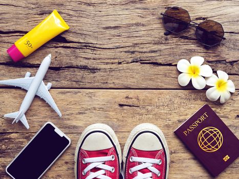 flat lay of passport , mobile , plane model , red sneakers and traveler's accessories items on wooden background with copy space. travel and vacation concept