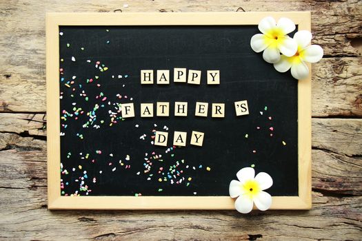 happy father's day word from wooden block place on black chalk board decorate with tropical flower on wooden background