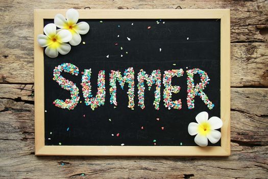 SUMMER word made from colorful gravel on black chalk board decorate with tropical flower on wooden background