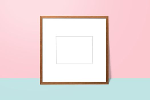 empty white space in wooden blank frame leaning against with pink wall and blue floor. simple blank photo frame for presentation or decorate background