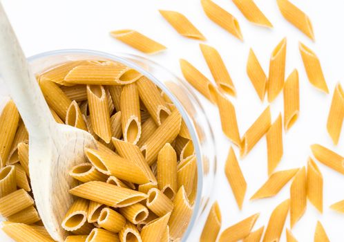 Close up of whole pasta in a glass bowl and wooden spoon on white background. Top view. Shallow depth of field.