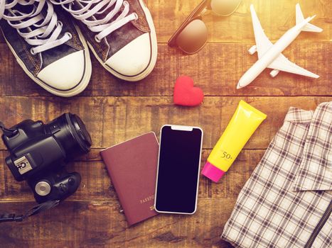 flat lay of passport ,mobile, plane model , sneakers , wallet , camera and traveler's accessories items on wooden background with copy space. travel and vacation concept