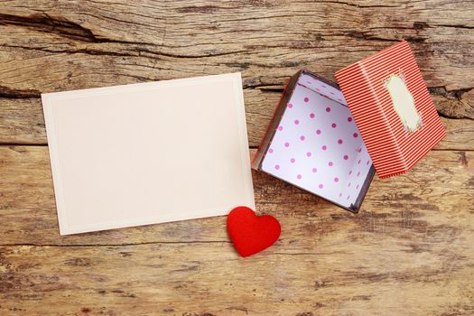 blank pink greeting card with border frame and empty red present gift box with open cover, decorate with red heart on wooden background