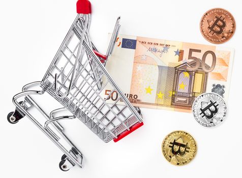 50 Euro and physical metal bitcoins ( gold, silver, bronze) in fallen toy trolley. Business concept, wrong investment, crisis. Traditional money versus cryptocurrency concept.