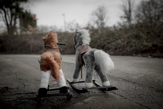 Two toy horses lie abandoned on the roadside.