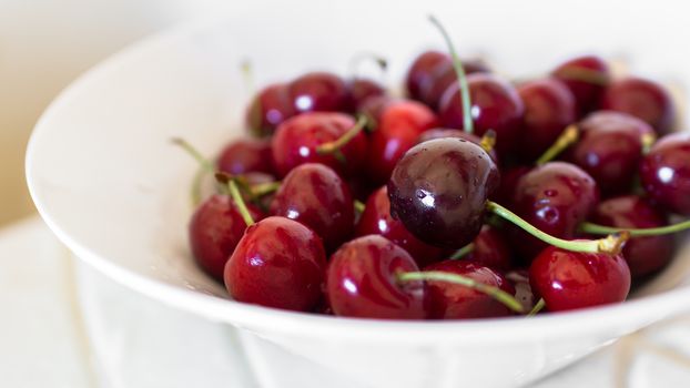 Ripe cherries on a white plate, isolated on background out of focus.