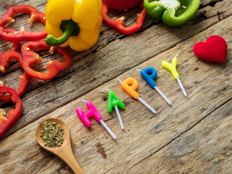 flat lay of cooking utensils with herbs , colorful bell pepper and word happy from candles over wooden background. top view with copy space. enjoy eating food and cooking concept