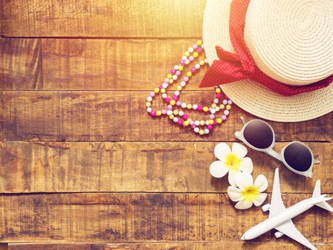 flat lay of hat , necklace , sun glass , flower and red heart shape as traveler's accessories items for summer vacation and plane model on wooden background with copy space. love travel and vacation