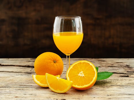 a glass of fresh orange juice and group of fresh orange fruits with green leaves, on wooden background. fruit product display or montage, studio shot