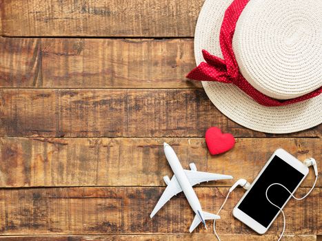 flat lay of plane model , red heart shape ,mobile ,earphone and woman hat as traveler's accessories items on wooden background with copy space inside colorful bead frame. travel and vacation for girl