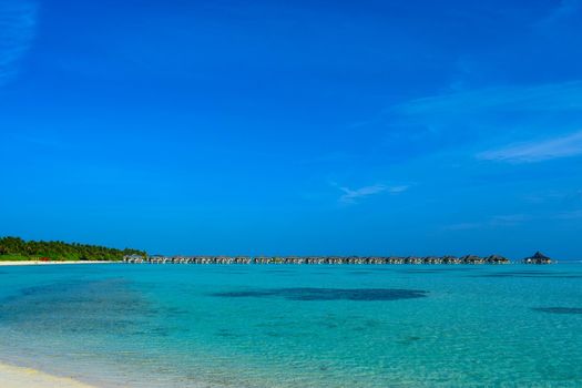 Sunny beach with white sand, coconut palm trees and turquoise sea. Summer vacation and tropical beach concept. Overwater at Maldive Island resort.