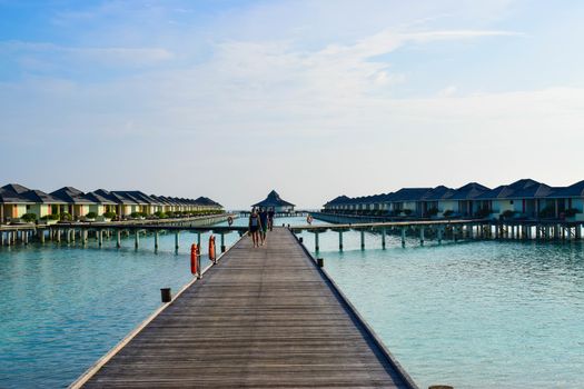 Sunny beach with white sand, coconut palm trees and turquoise sea. Summer vacation and tropical beach concept. Overwater at Maldive Island resort.