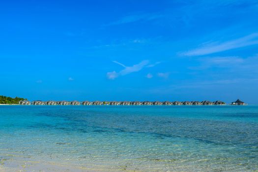 Sunny beach with white sand, coconut palm trees and turquoise sea. Summer vacation and tropical beach concept. Overwater at Maldive Island resort.