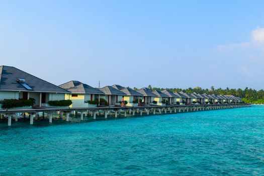 Sunny beach with white sand, coconut palm trees and turquoise sea. Summer vacation and tropical beach concept. Overwater at Maldive Island resort.