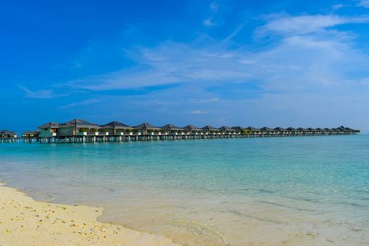 Sunny beach with white sand, coconut palm trees and turquoise sea. Summer vacation and tropical beach concept. Overwater at Maldive Island resort.