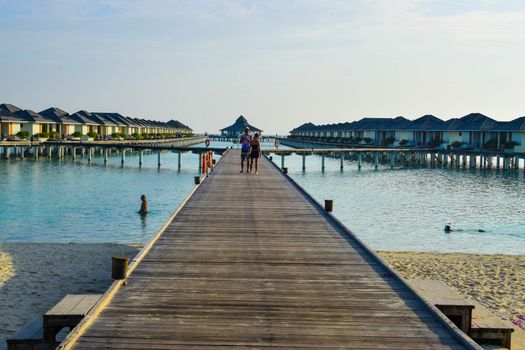 Sunny beach with white sand, coconut palm trees and turquoise sea. Summer vacation and tropical beach concept. Overwater at Maldive Island resort.