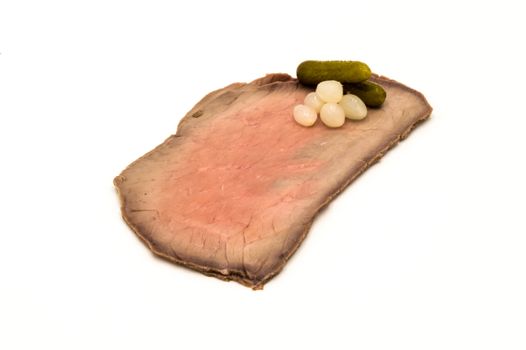 slices of roast beef perfectly arranged with small onions and pickles on a white background