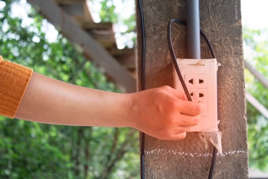 Close-up of Asian women' s hand is plugging in the socket . Dangerous situation in home.