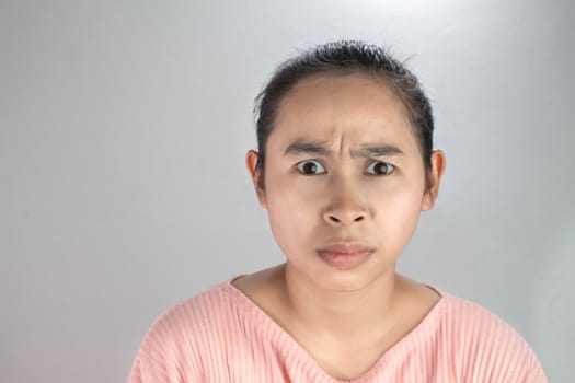 Portrait angry face of Asian young woman in pink shirt on grey background.