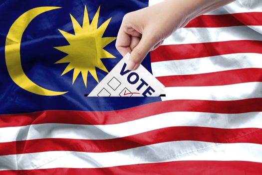 Malaysia general election concept. close up hand of a person casting a ballot at elections during voting on canvas Malaysia flag background.