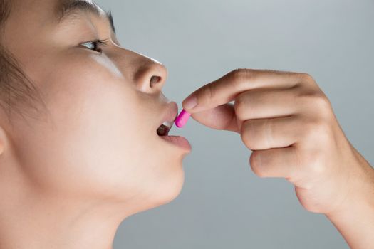 Close-up of Unhealthy sick Asian woman is putting Pink capsule pill in mouth. Female patient taking medicines.