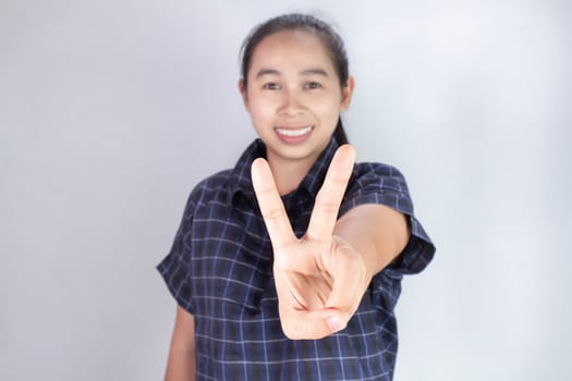 Portrait of Asian young woman in blue shirt, Showing outstretched hands with two fingers in victory gesture isolated on grey background. Body language and encouragement concept.