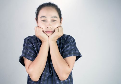 Portrait of young woman looking bored and put hands on chin isolated on a grey background.