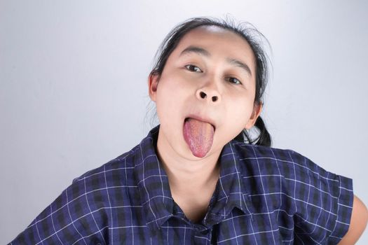 Asian young woman in blue shirt, Make funny faces and showing long tongue for you to be happy and not stressed. Body language and encouragement concept.