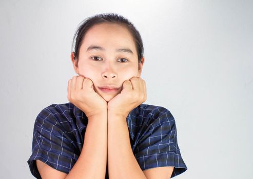 Portrait of young woman looking bored and put hands on chin isolated on a grey background.